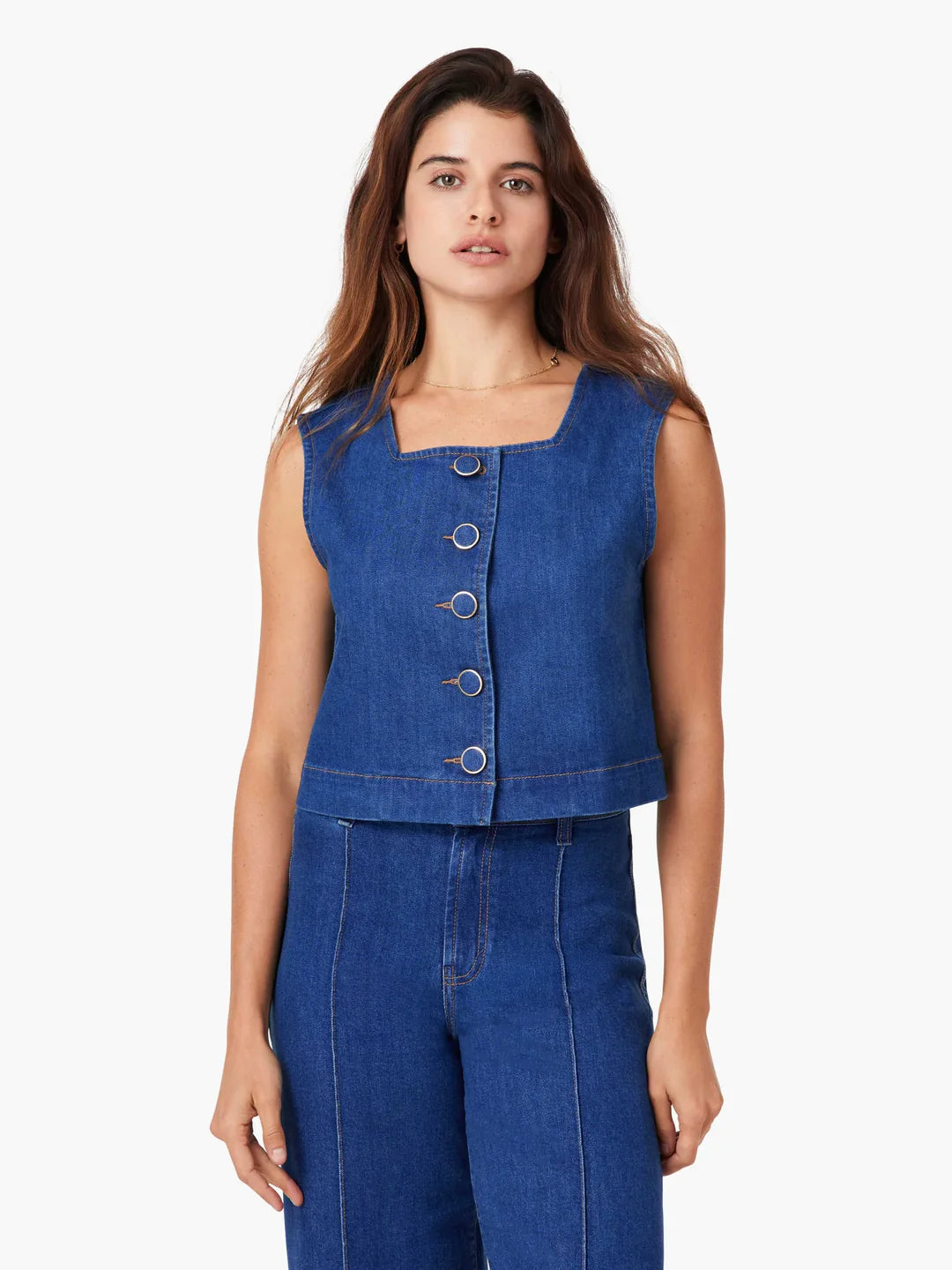 Woman wearing a blue sleeveless top with buttons in a studio setting