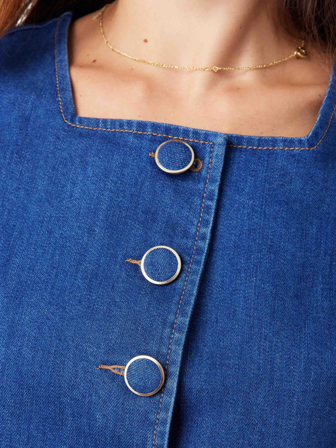 Close-up of a blue denim garment with gold buttons and a gold necklace.