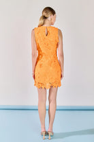 Woman wearing an orange lace dress standing against a plain background