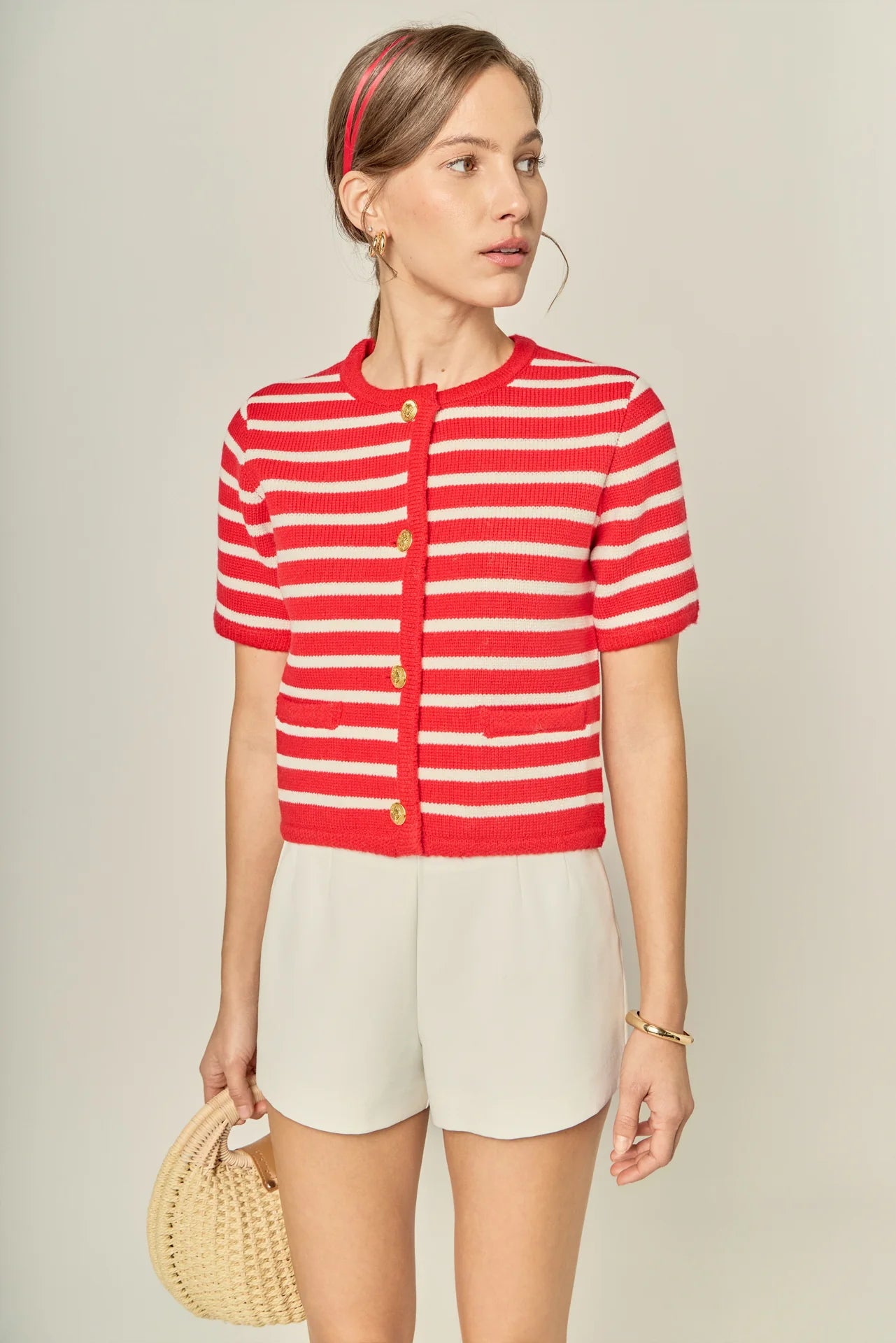 Woman wearing a red and white striped shirt with beige shorts, holding a woven bag.