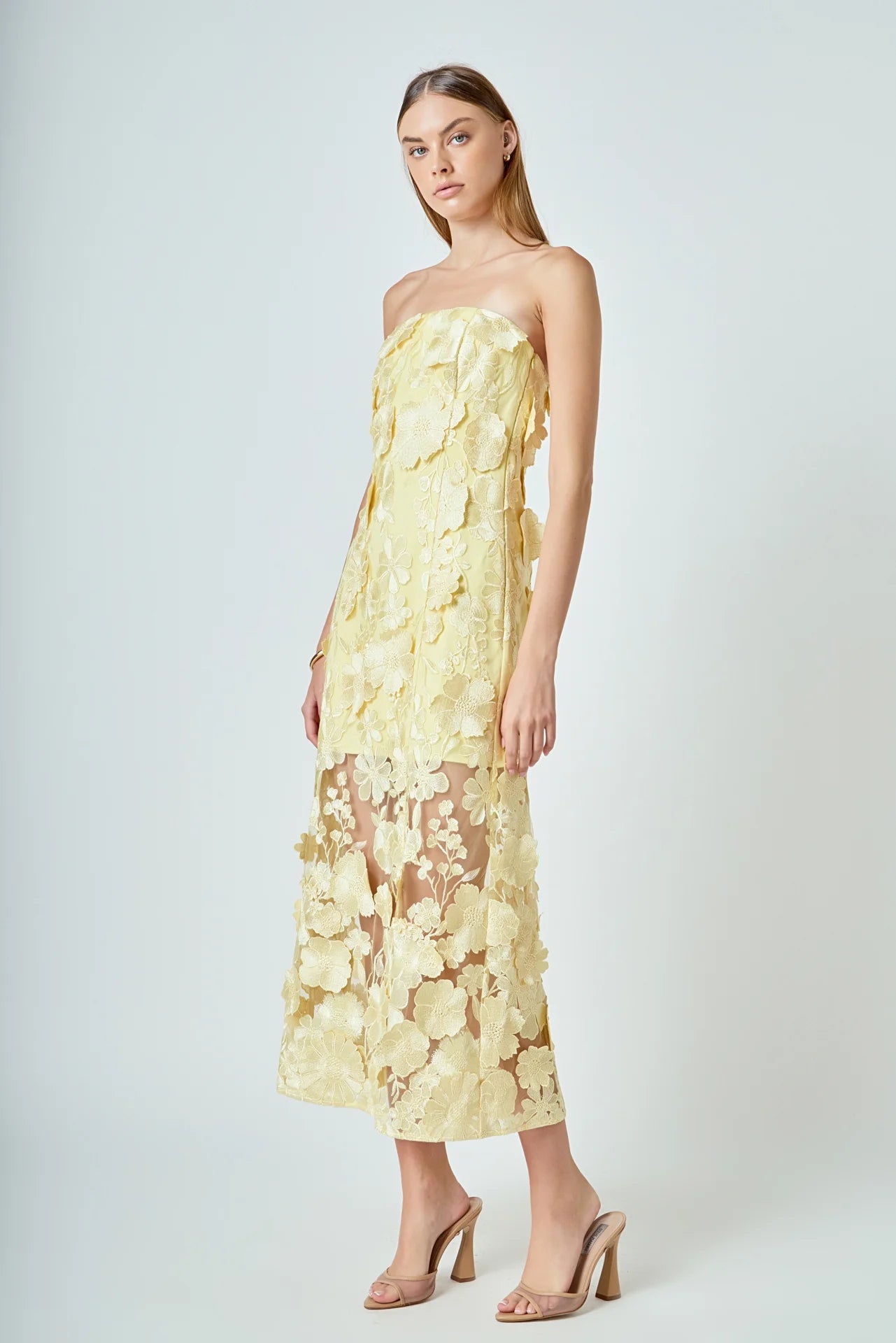 Woman wearing a yellow floral strapless dress on a white background