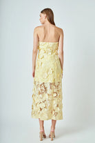 Woman wearing a yellow strapless dress with floral lace details on a white background