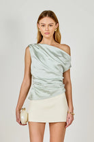 Woman wearing a light green off-shoulder top and beige skirt on a plain background
