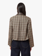 A model shown from the back wearing a cropped plaid blazer with a dark brown leather collar, paired with dark blue jeans, against a plain white background.