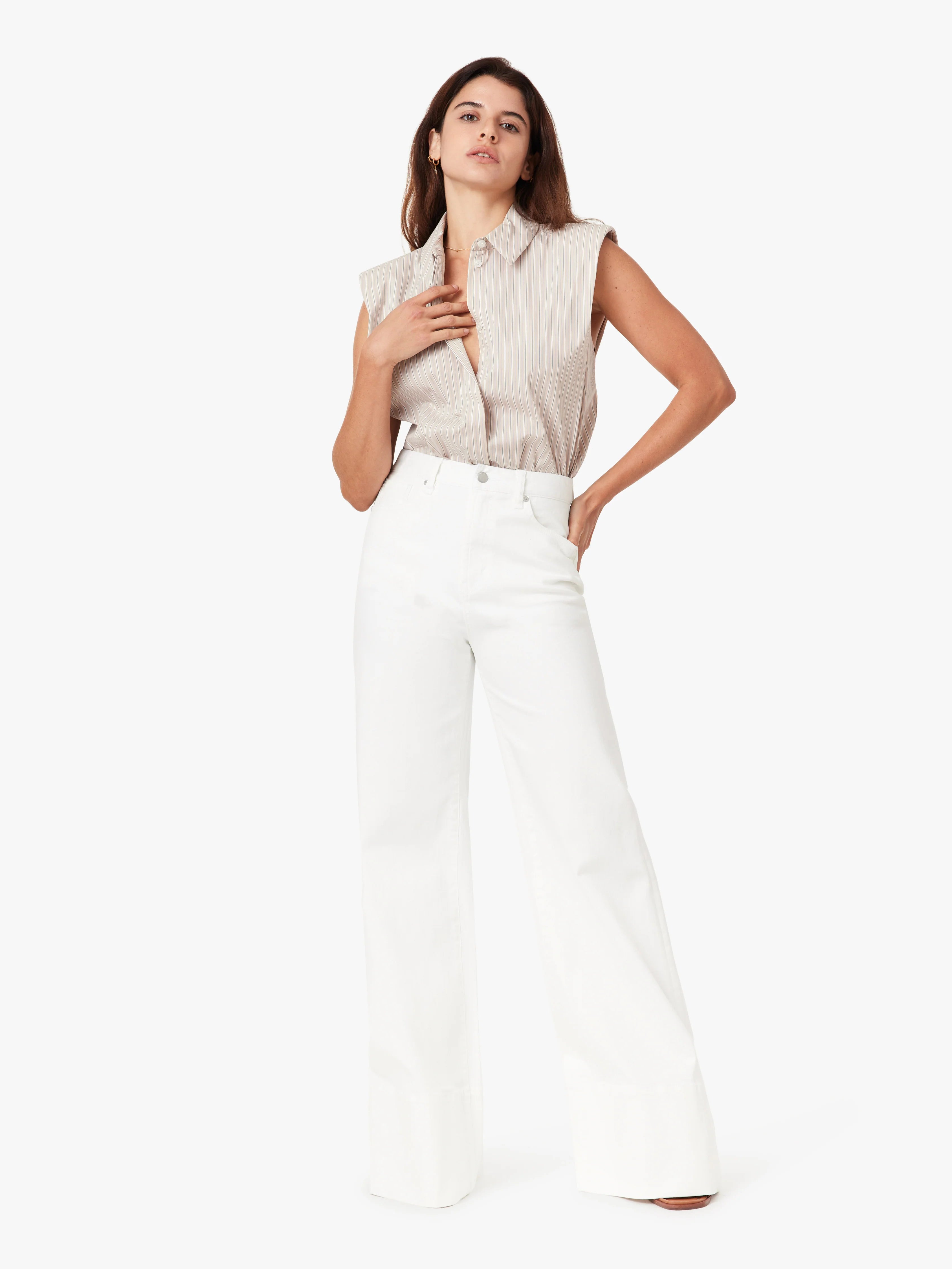 Woman wearing a sleeveless beige top and white pants on a white background
