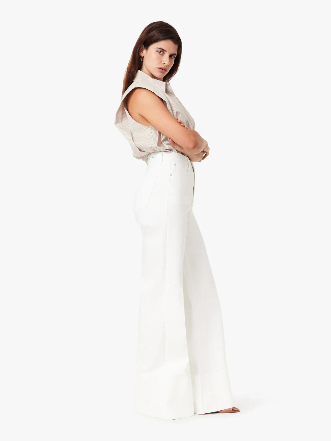 Woman wearing a beige sleeveless top and white pants on a white background