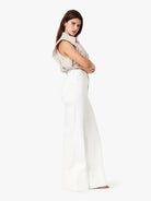 Woman wearing a beige sleeveless top and white pants on a white background