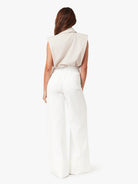 Woman wearing a beige sleeveless top and white pants on a white background