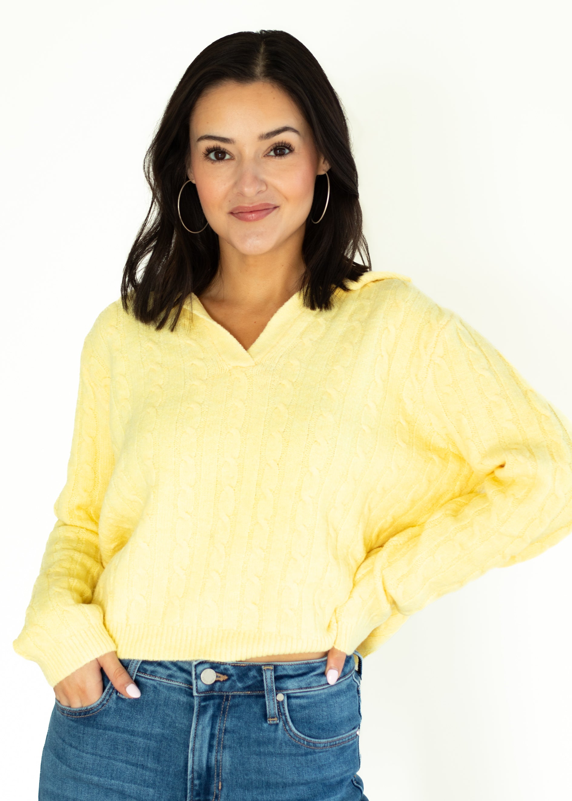 Woman wearing a yellow sweater and blue jeans on a white background