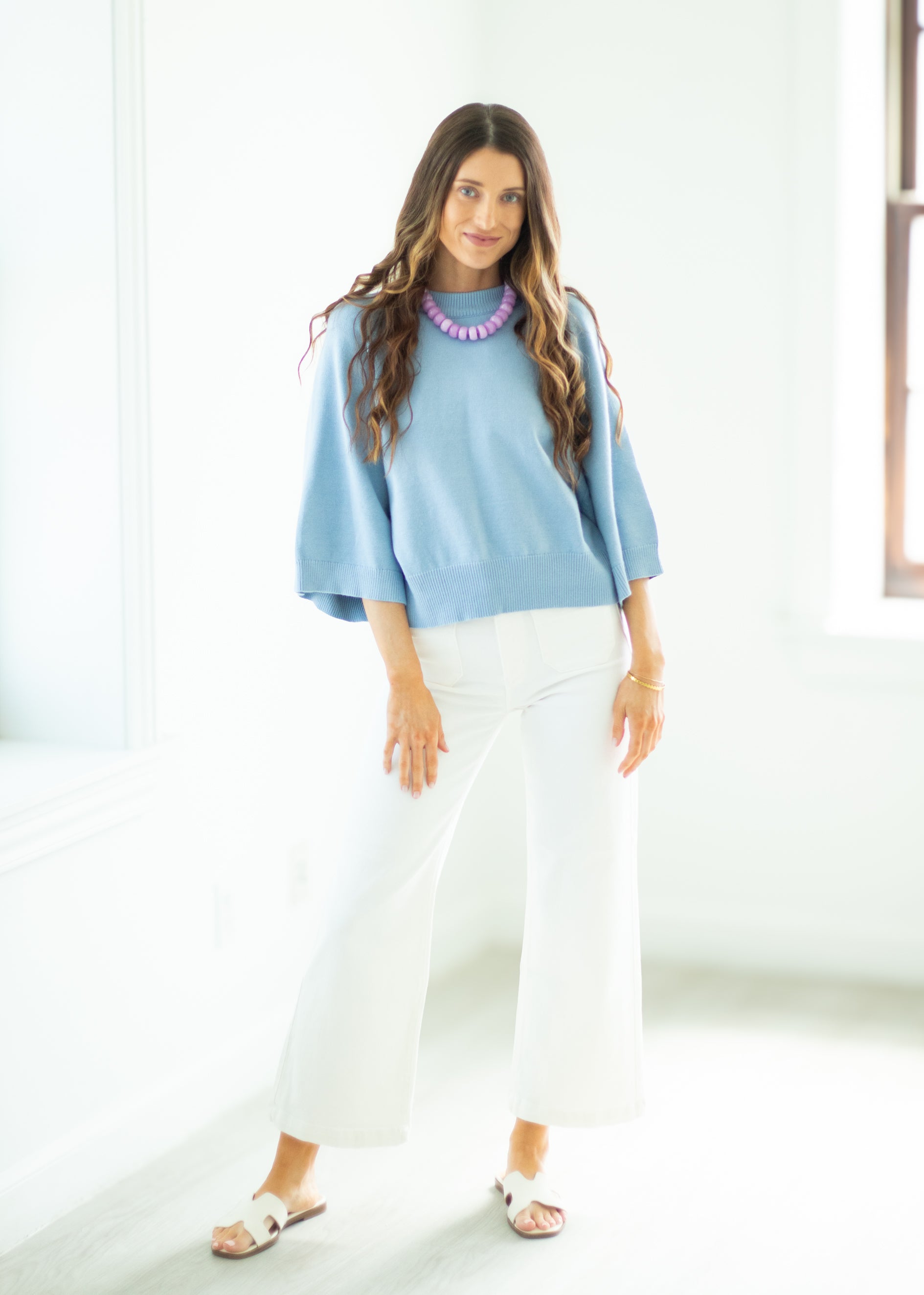 Woman wearing a light blue sweater and white pants in a bright room