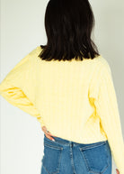 Person wearing a yellow long-sleeve top and blue jeans against a plain background