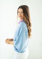 Woman wearing a light blue sweater and white pants with a white background
