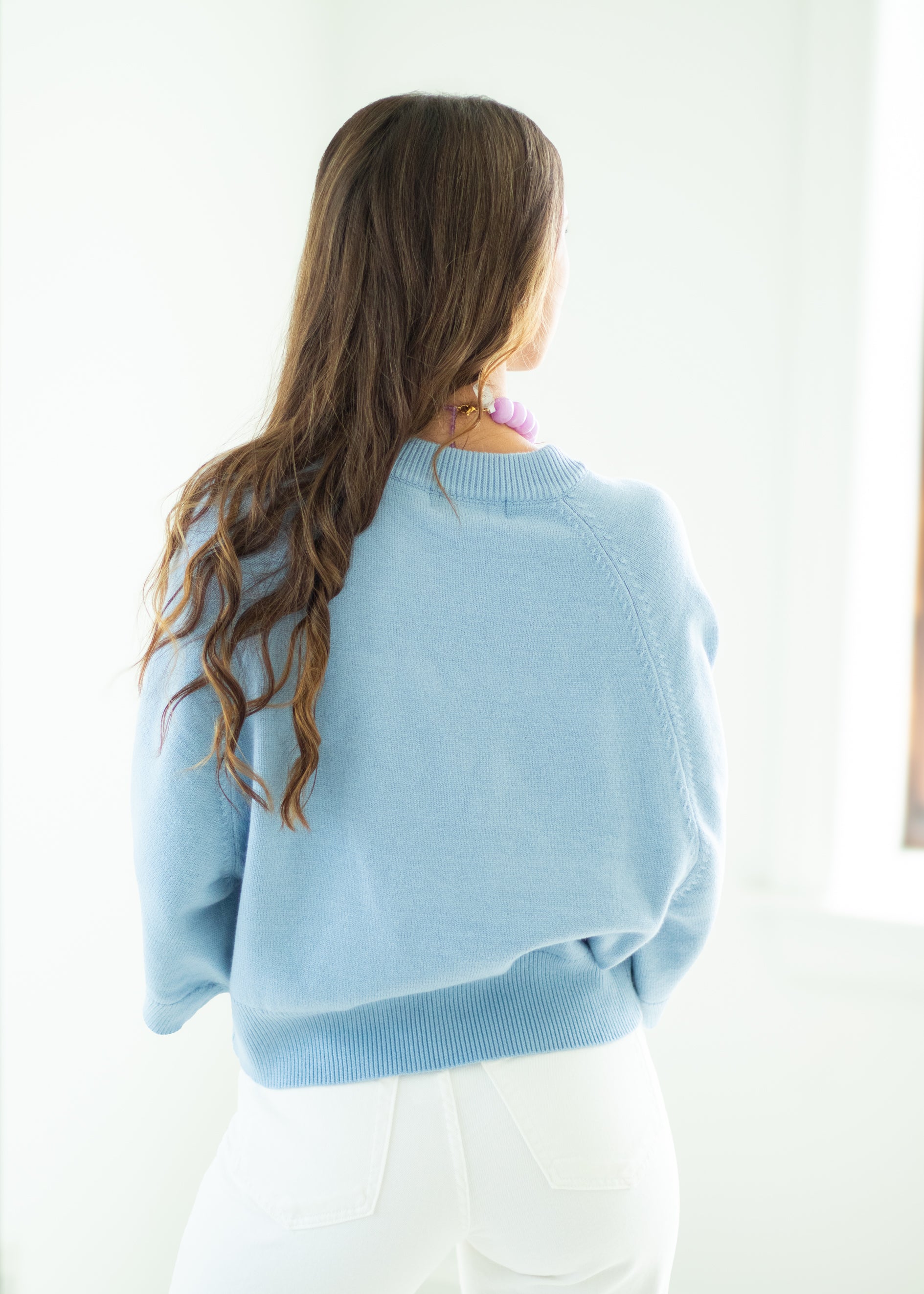 Woman wearing a light blue sweater and white pants against a white background