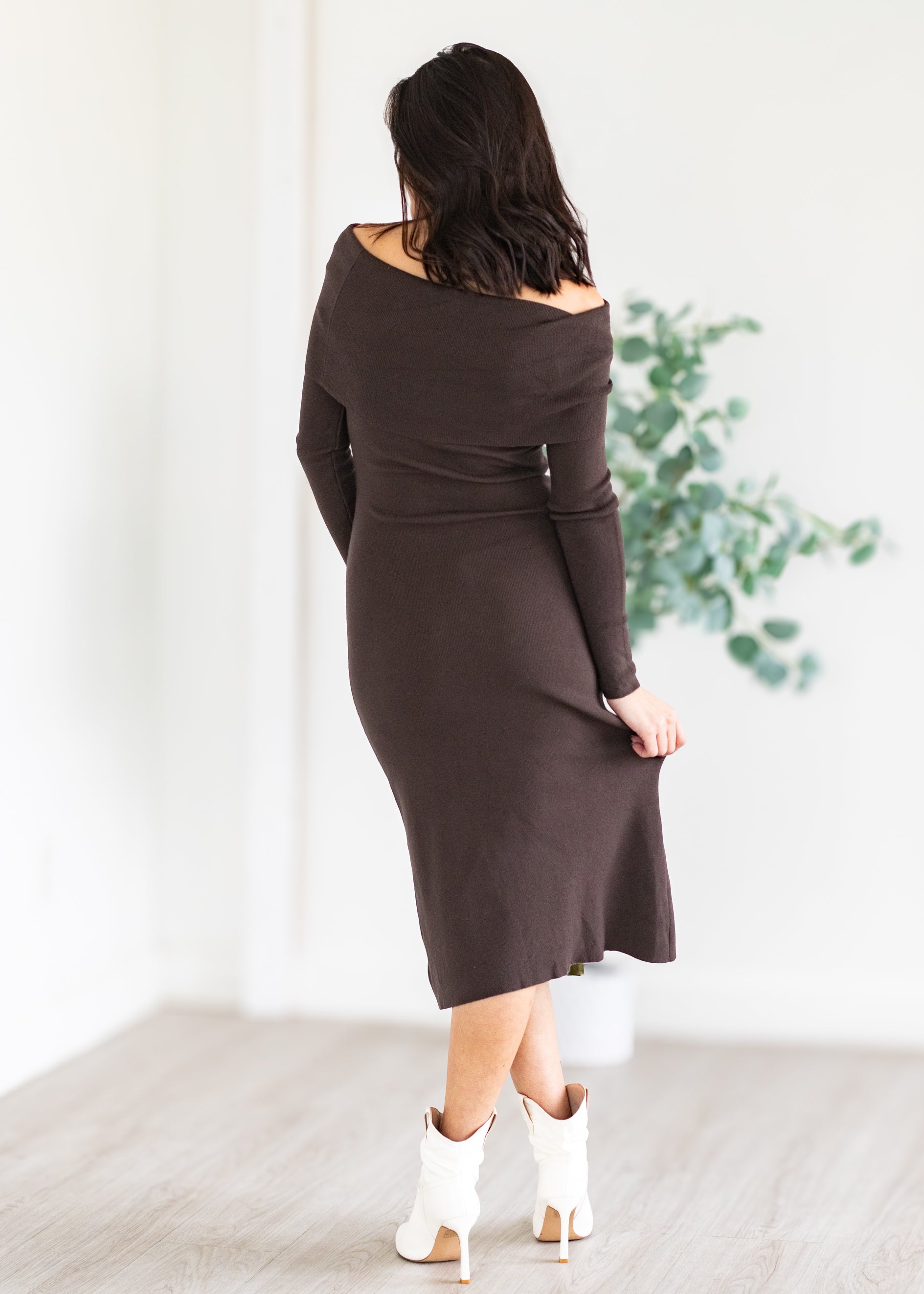Woman wearing a brown dress with long sleeves in a minimal indoor setting.