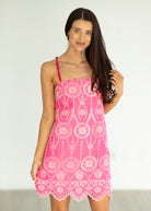 Woman wearing a pink dress with white patterns on a plain background