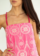 Woman wearing a pink dress with white floral pattern and red straps on a plain background
