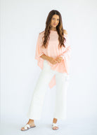 Woman wearing a peach top and white pants on a white background