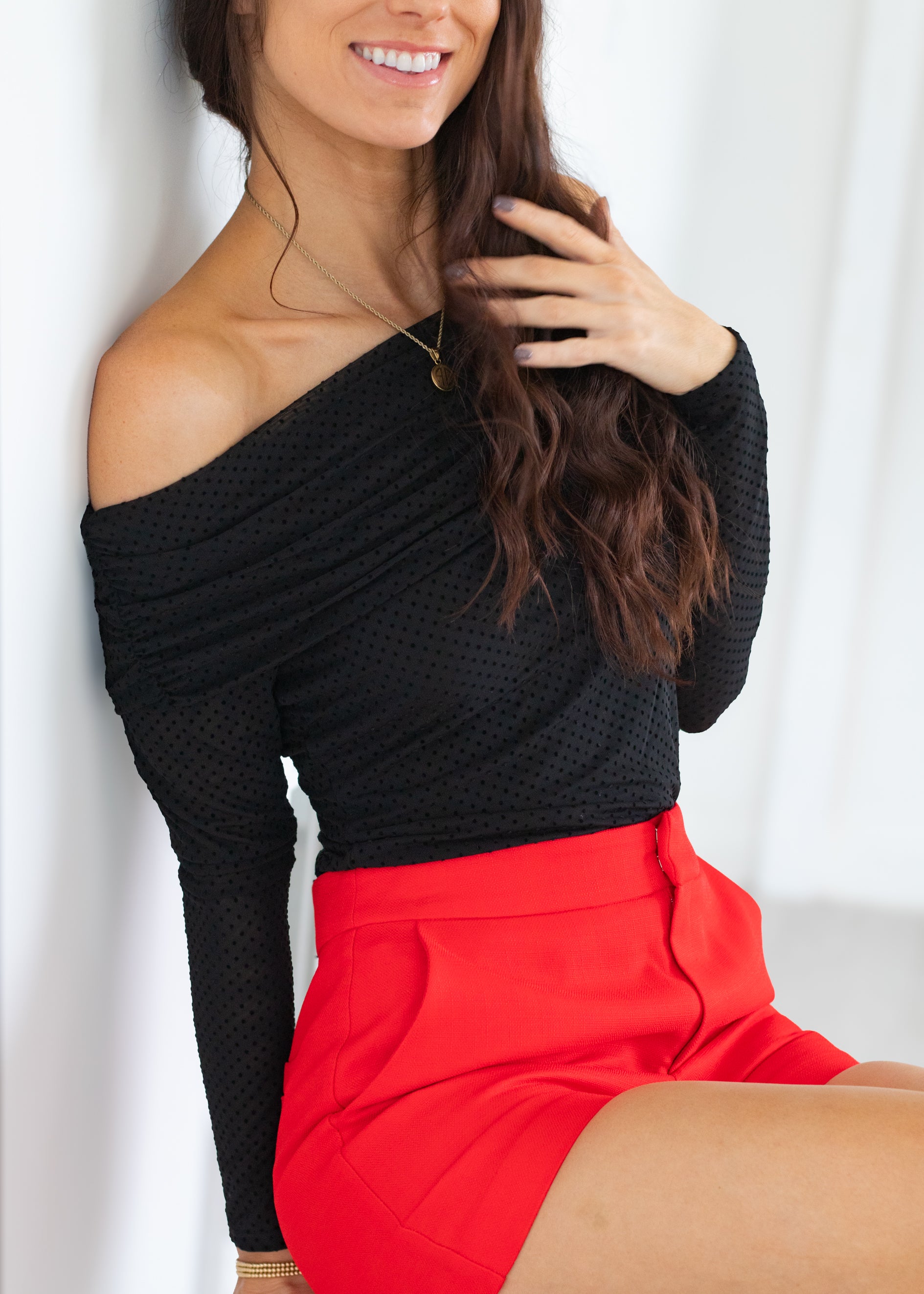 Woman wearing a black one-shoulder top and red shorts against a white background