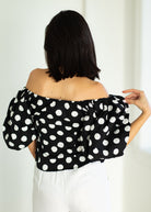 Woman wearing a black off-shoulder top with white polka dots against a white background
