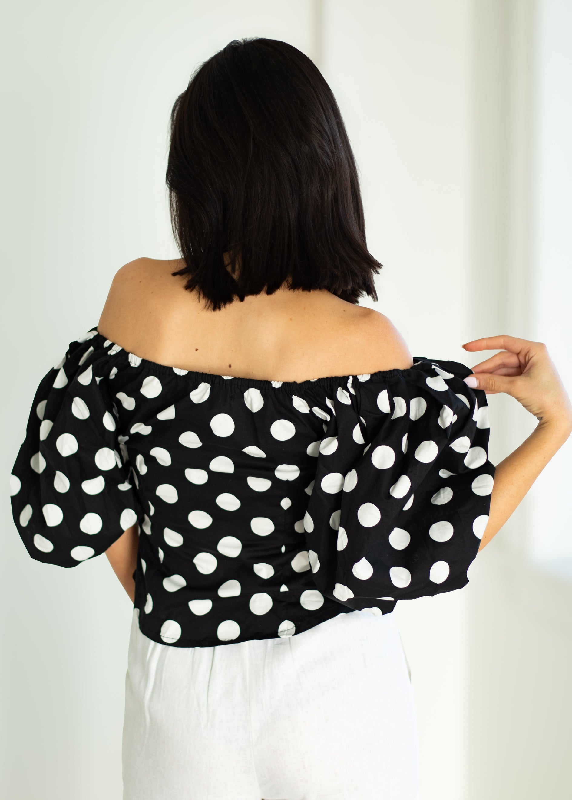 Woman wearing a black off-shoulder top with white polka dots against a white background