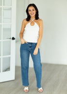 Woman wearing a white top and blue jeans standing in a room with a white door.