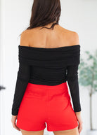 Person wearing a black off-shoulder top and red shorts against a white background