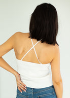 Person wearing a white tank top with thin straps on a plain background