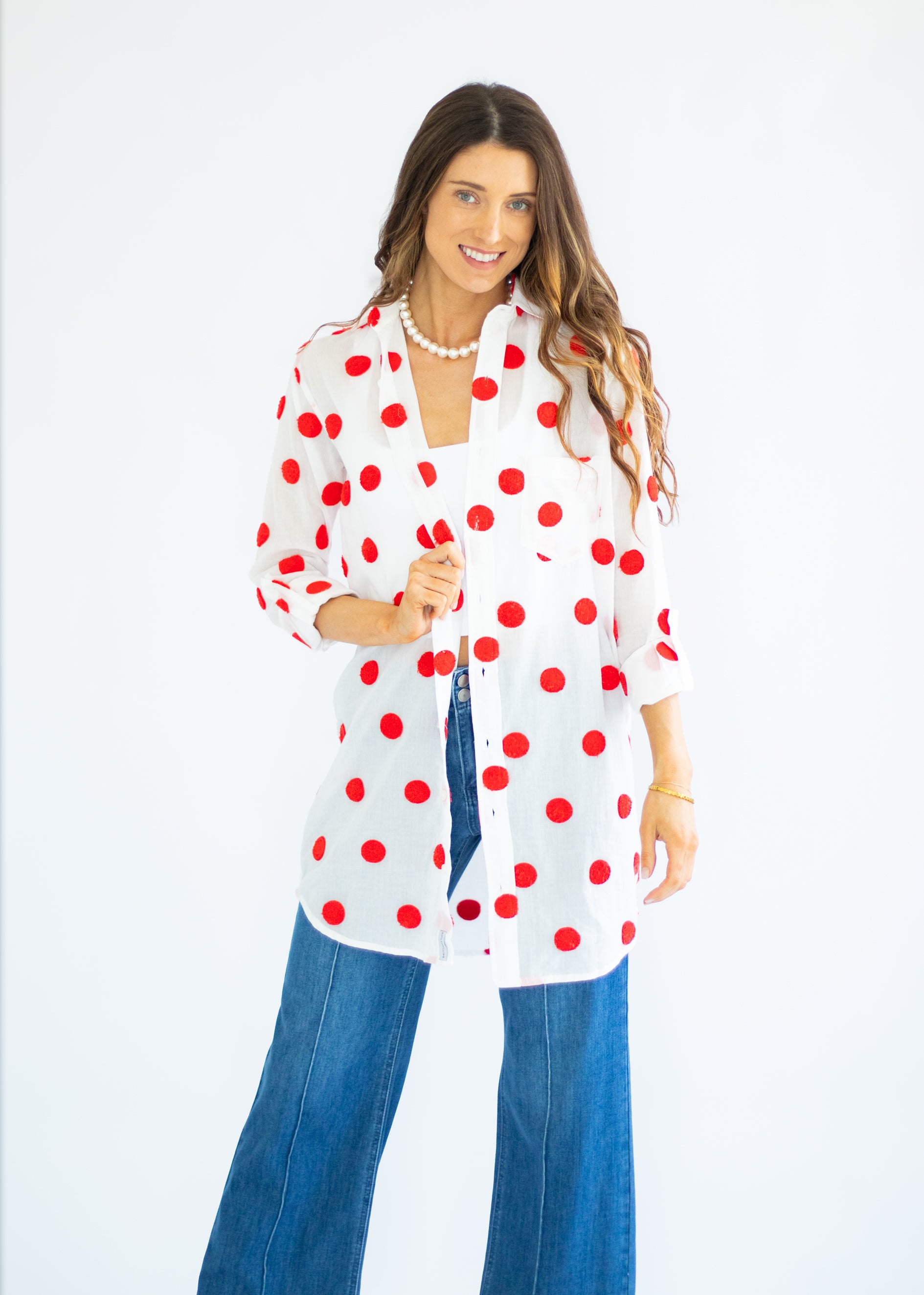 Woman wearing a white shirt with red polka dots and blue jeans on a white background