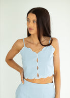 Woman wearing a light blue scalloped top against a white background