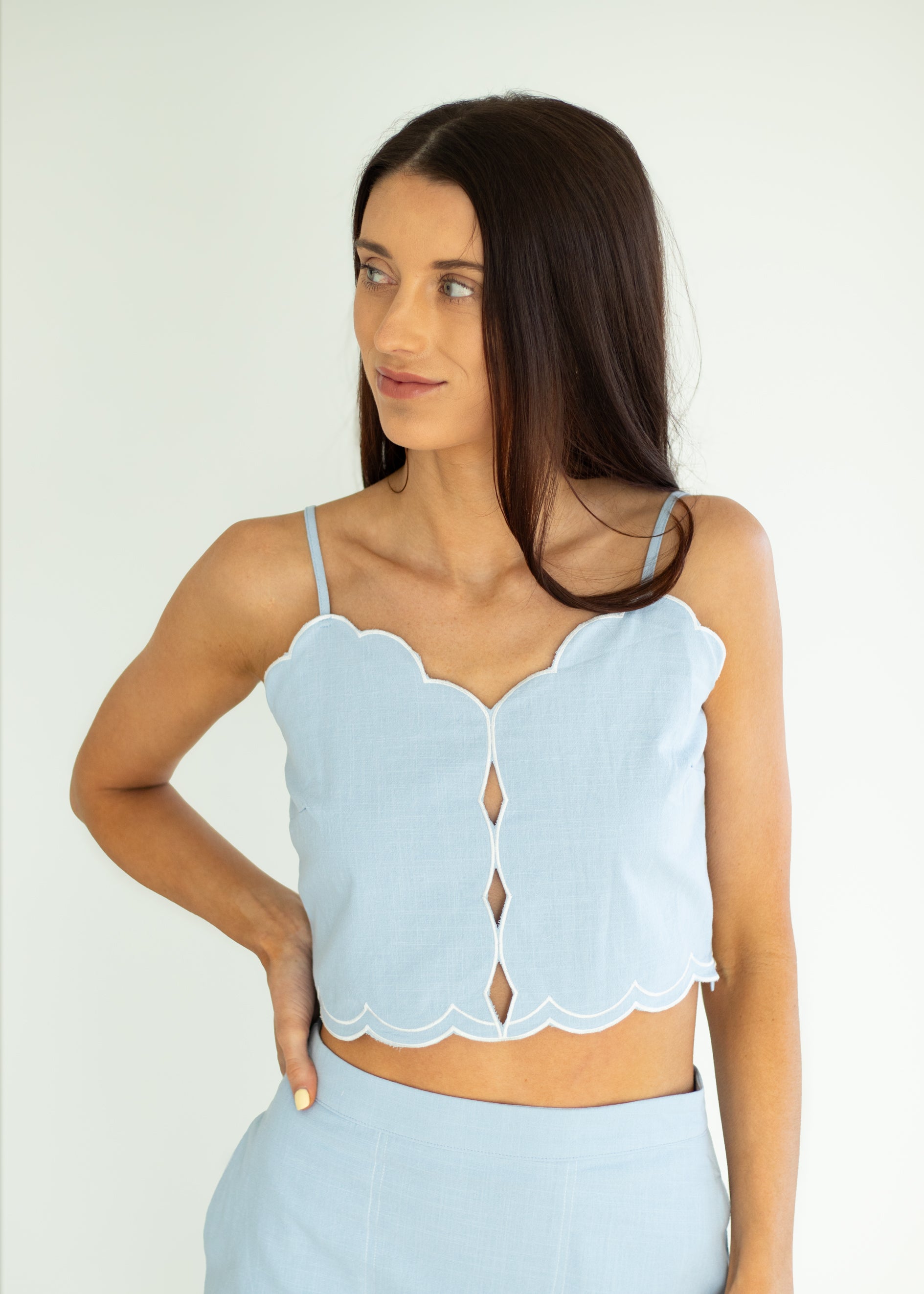 Woman wearing a light blue scalloped top against a white background