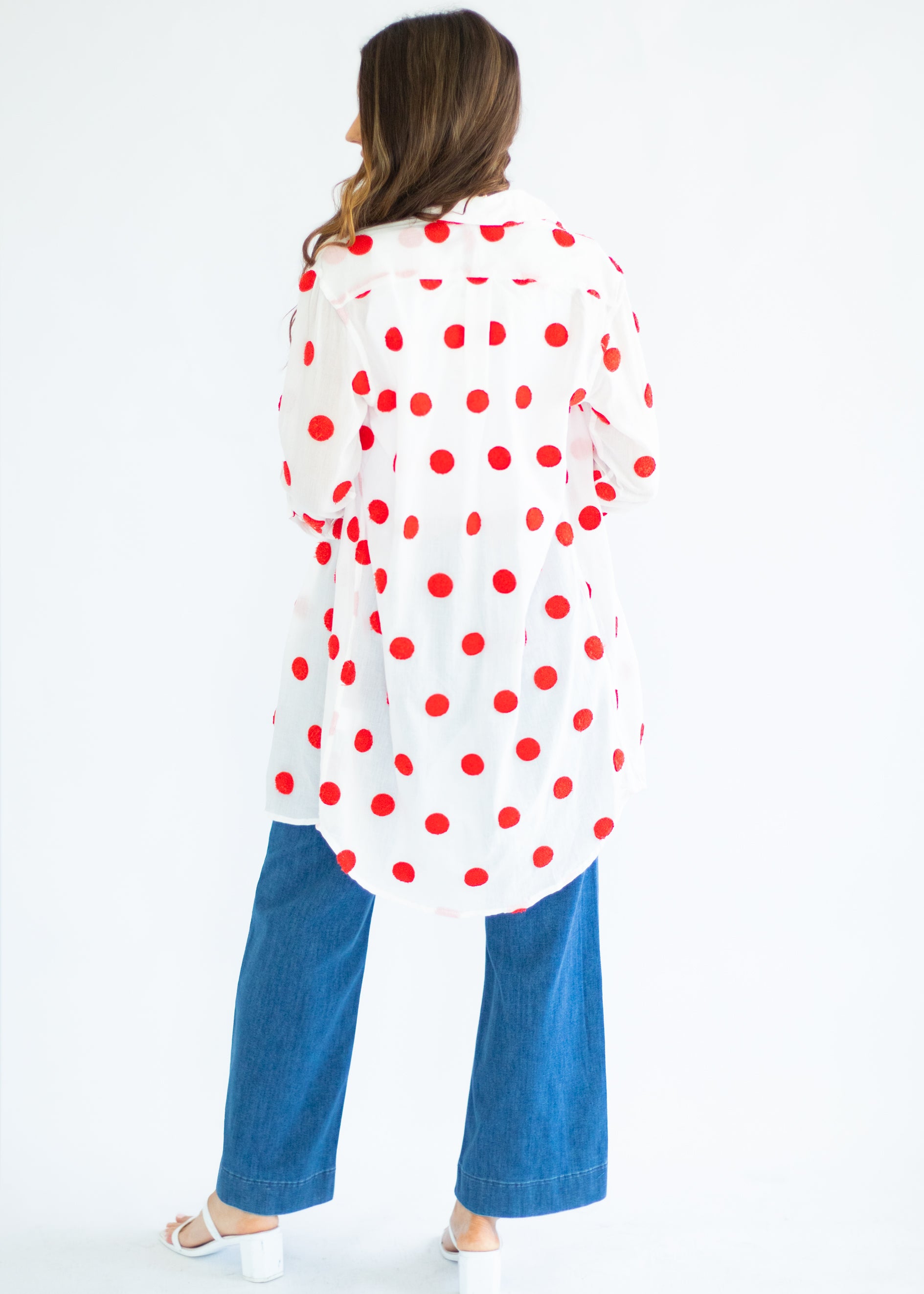 Woman wearing a white kimono-style garment with red polka dots and blue pants on a white background