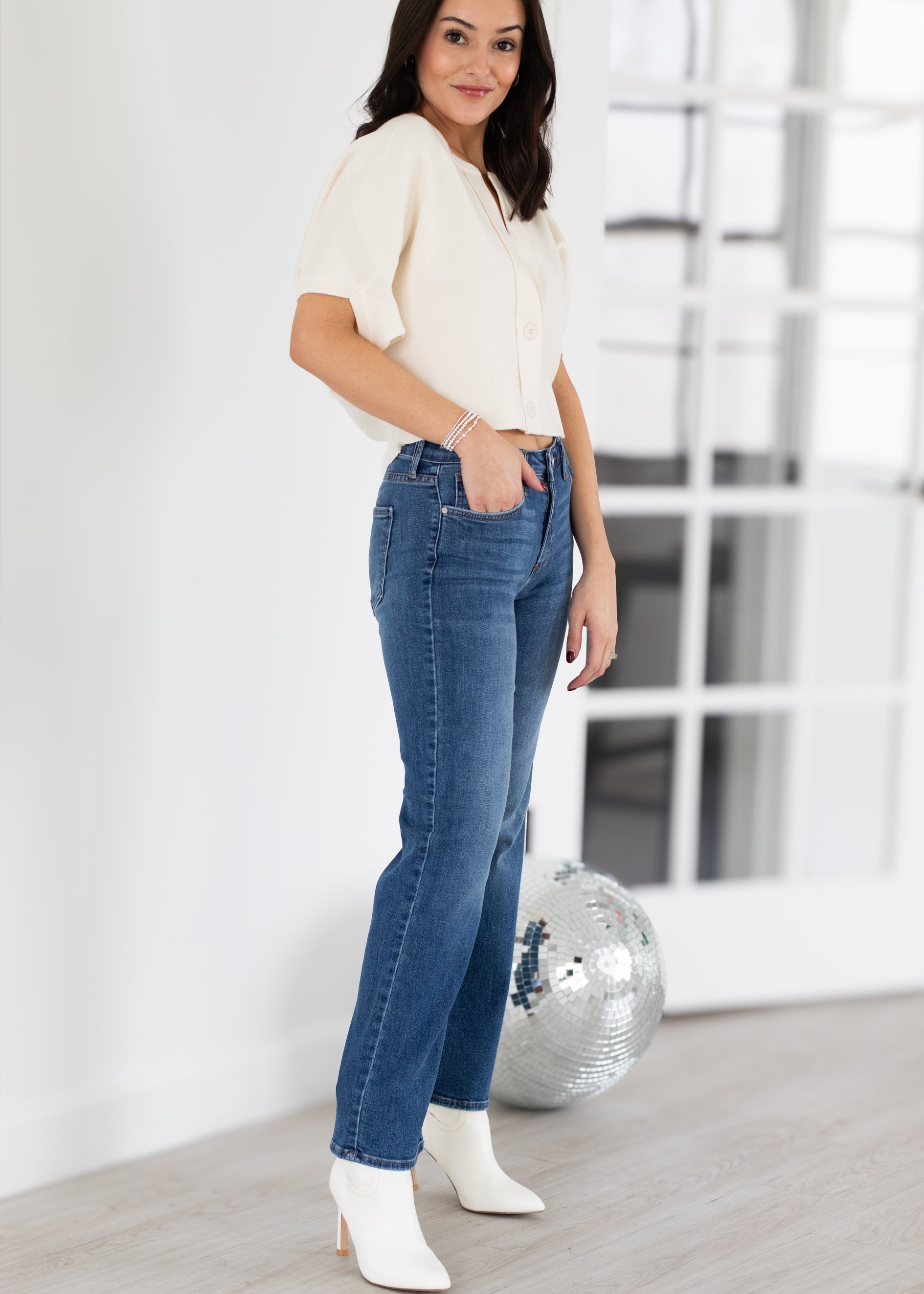 Woman wearing a white top and blue jeans with white shoes in a minimalistic room.