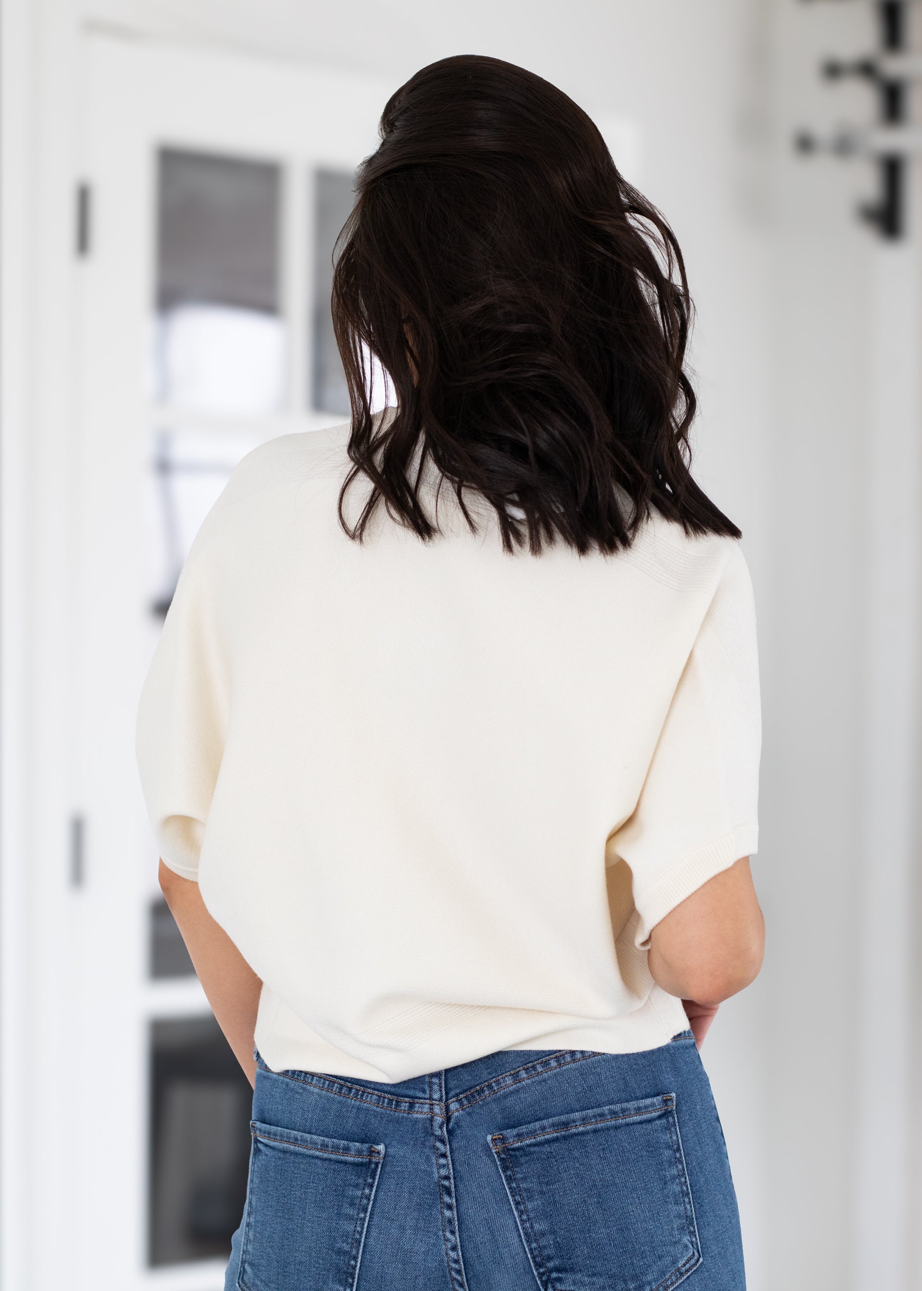 Person wearing a white top and blue jeans from behind in an indoor setting