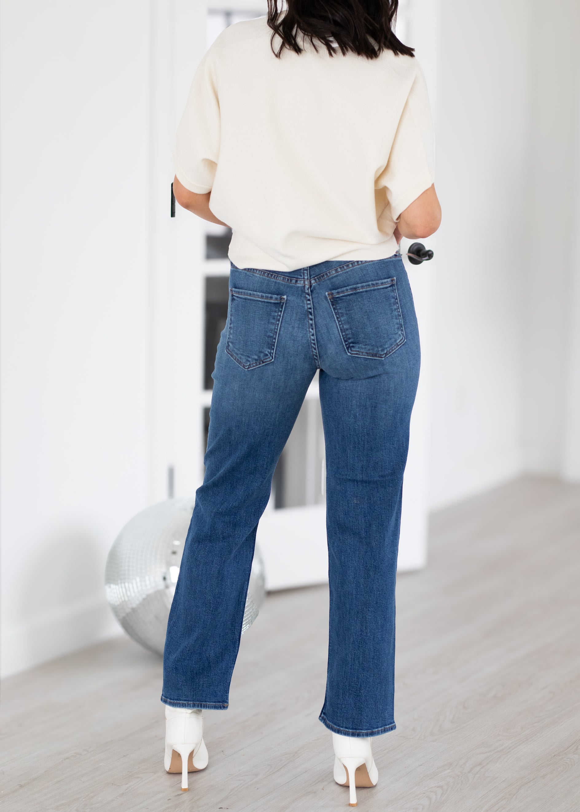 Person wearing blue jeans and a white top in a minimalistic room.