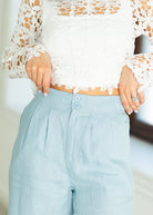 Person wearing a white lace top and light blue pants with a blurred background