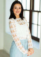 Woman wearing a white lace long-sleeve top and light blue jeans indoors.