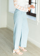 Person wearing light blue pants and a floral blouse in a minimal indoor setting.