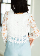 Person wearing a white lace top with long sleeves and light blue pants.