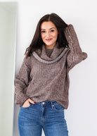 Woman wearing a brown ribbed sweater and blue jeans against a white background