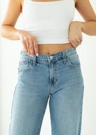Person wearing light blue jeans and a white crop top on a plain background