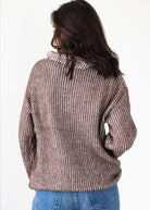 Person wearing a brown ribbed sweater and blue jeans on a white background