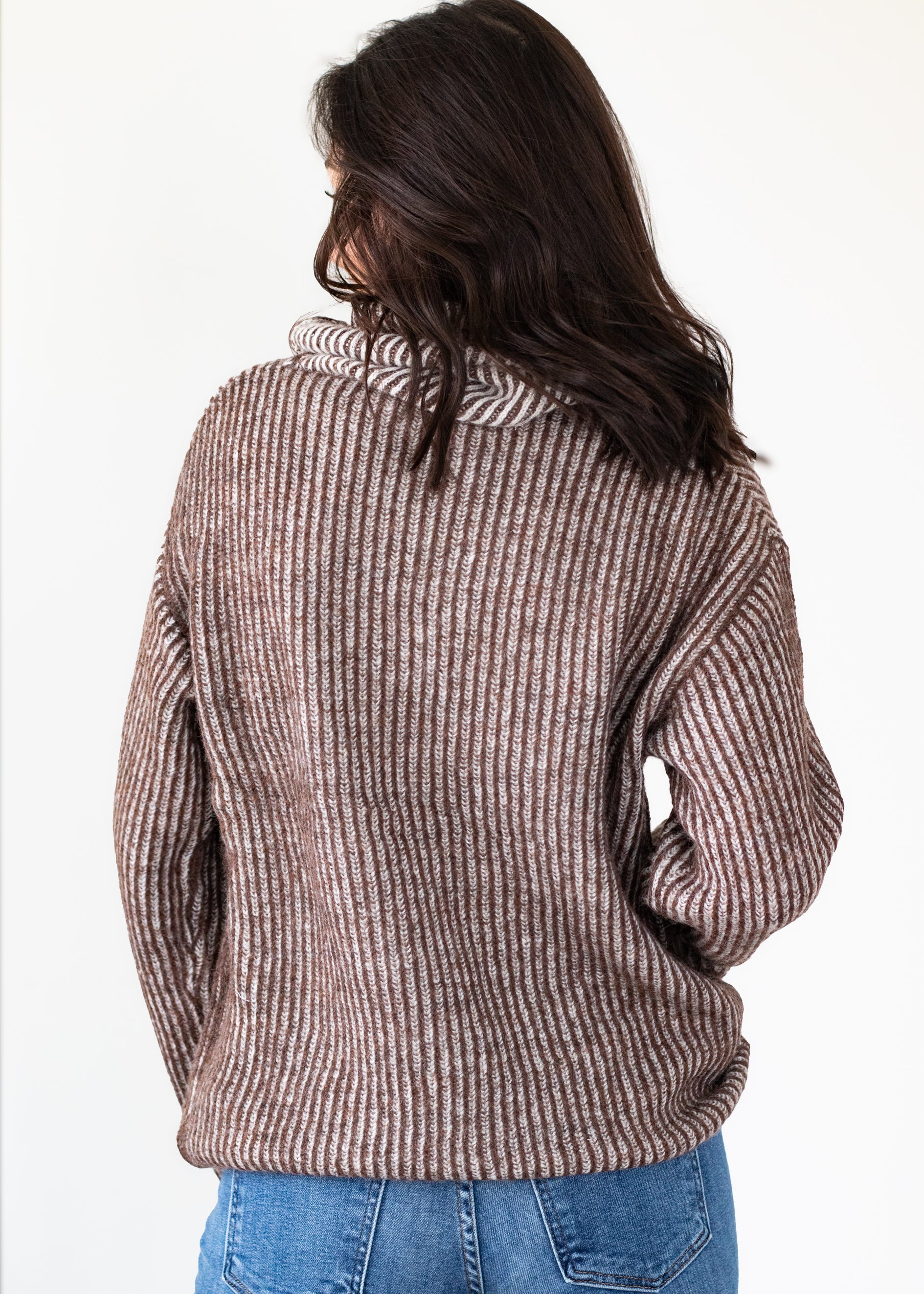 Person wearing a brown ribbed sweater and blue jeans on a white background