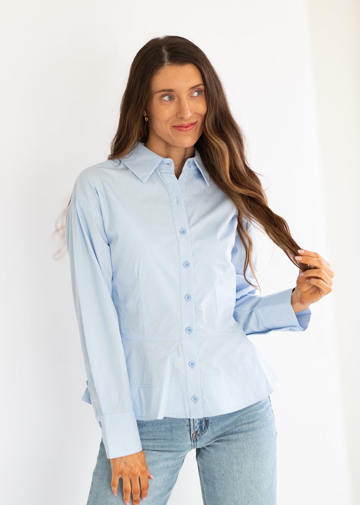 A woman modeling a light blue long-sleeve button-up shirt with light-wash blue jeans against a plain white studio background.