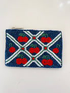 A small rectangular beaded coin purse with a zipper closure, featuring a navy blue background, red cherries with green stems, and white and green beaded geometric lines.