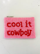 A pink beaded zipper pouch with red beaded text reading 'cool it cowboy' on a white background.