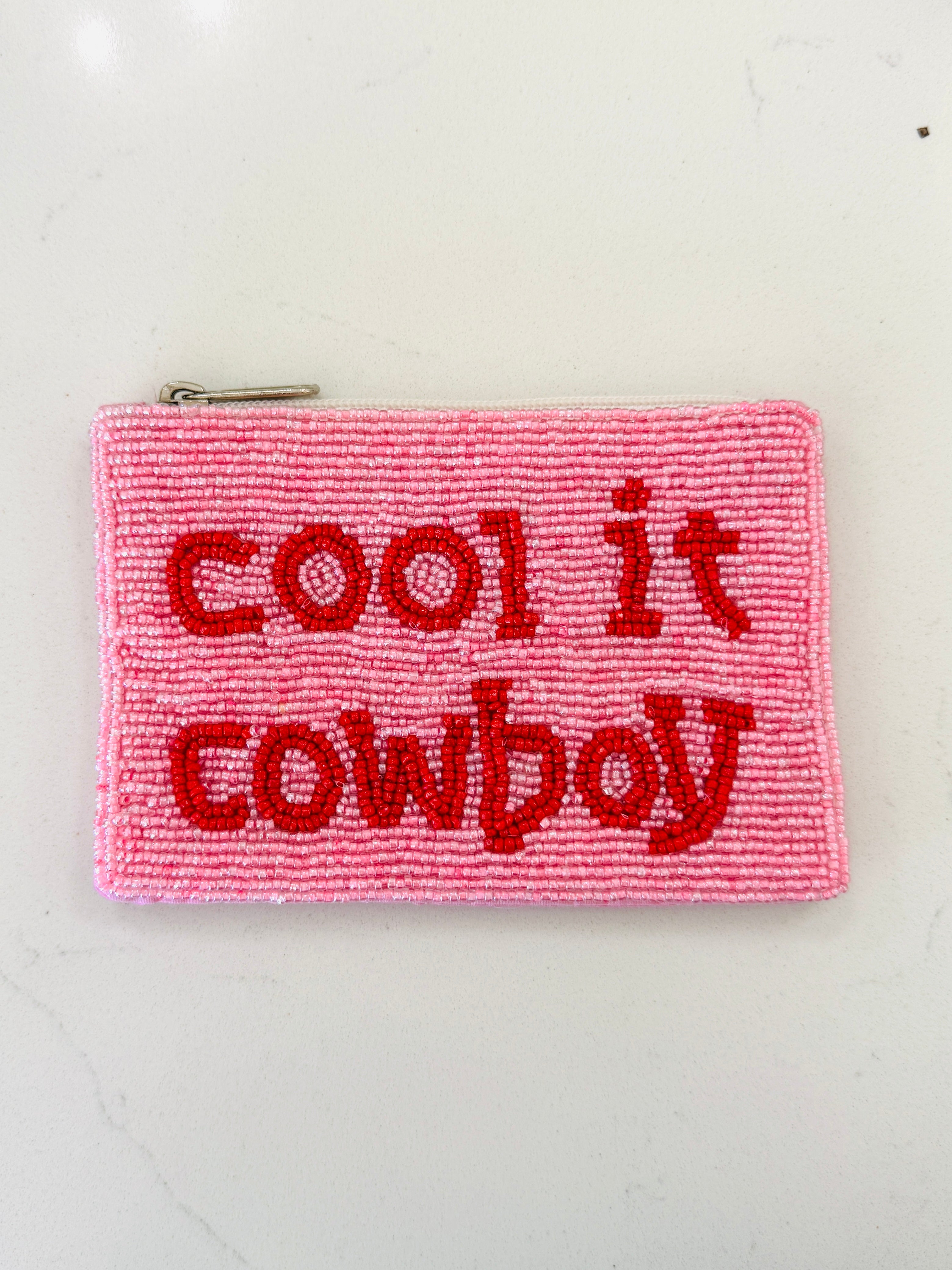 A pink beaded zipper pouch with red beaded text reading 'cool it cowboy' on a white background.