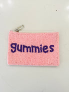 A pink textured zippered pouch with the word 'gummies' embroidered in dark purple across the front, shown on a light off-white background.
