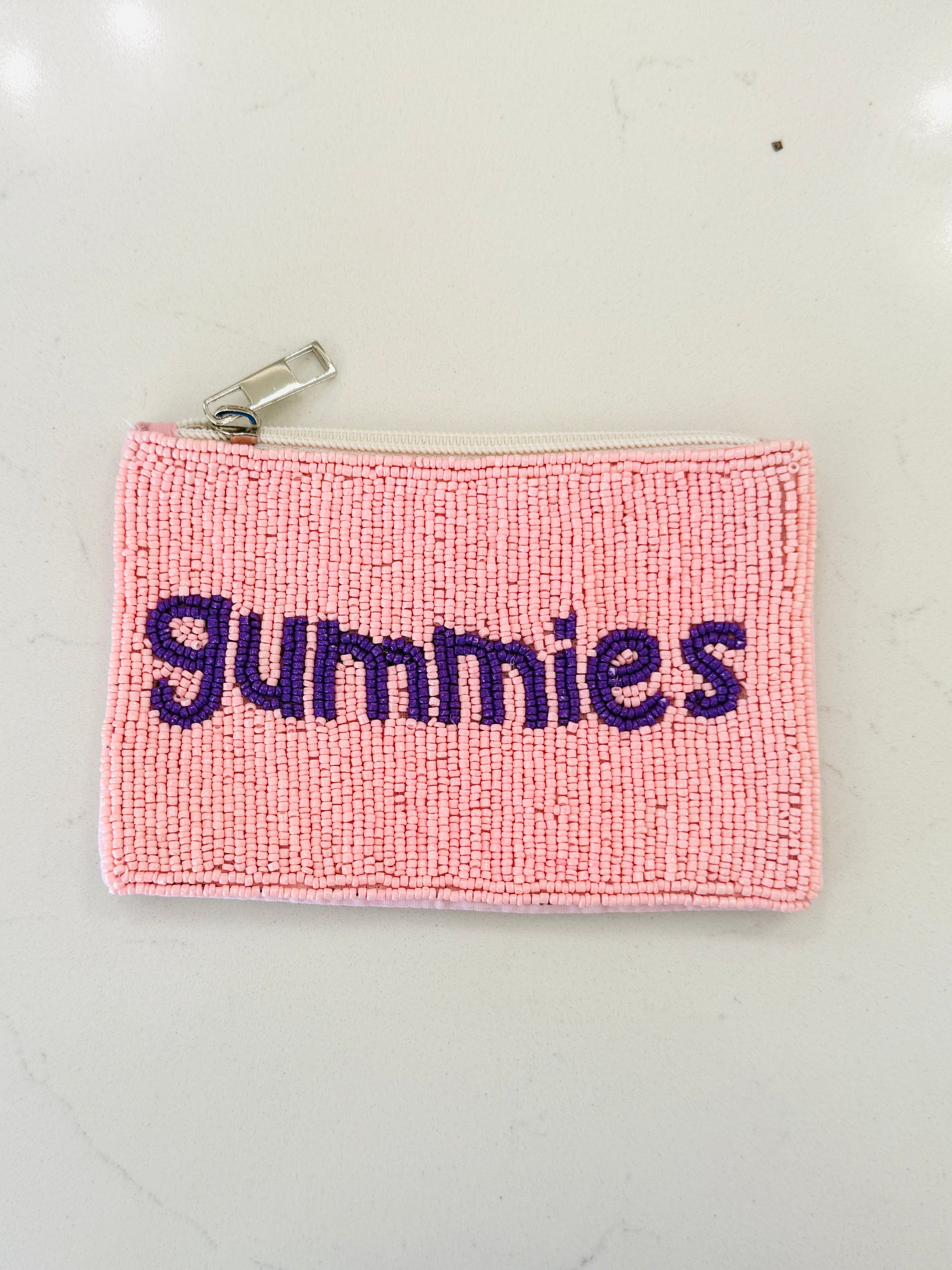 A pink textured zippered pouch with the word 'gummies' embroidered in dark purple across the front, shown on a light off-white background.