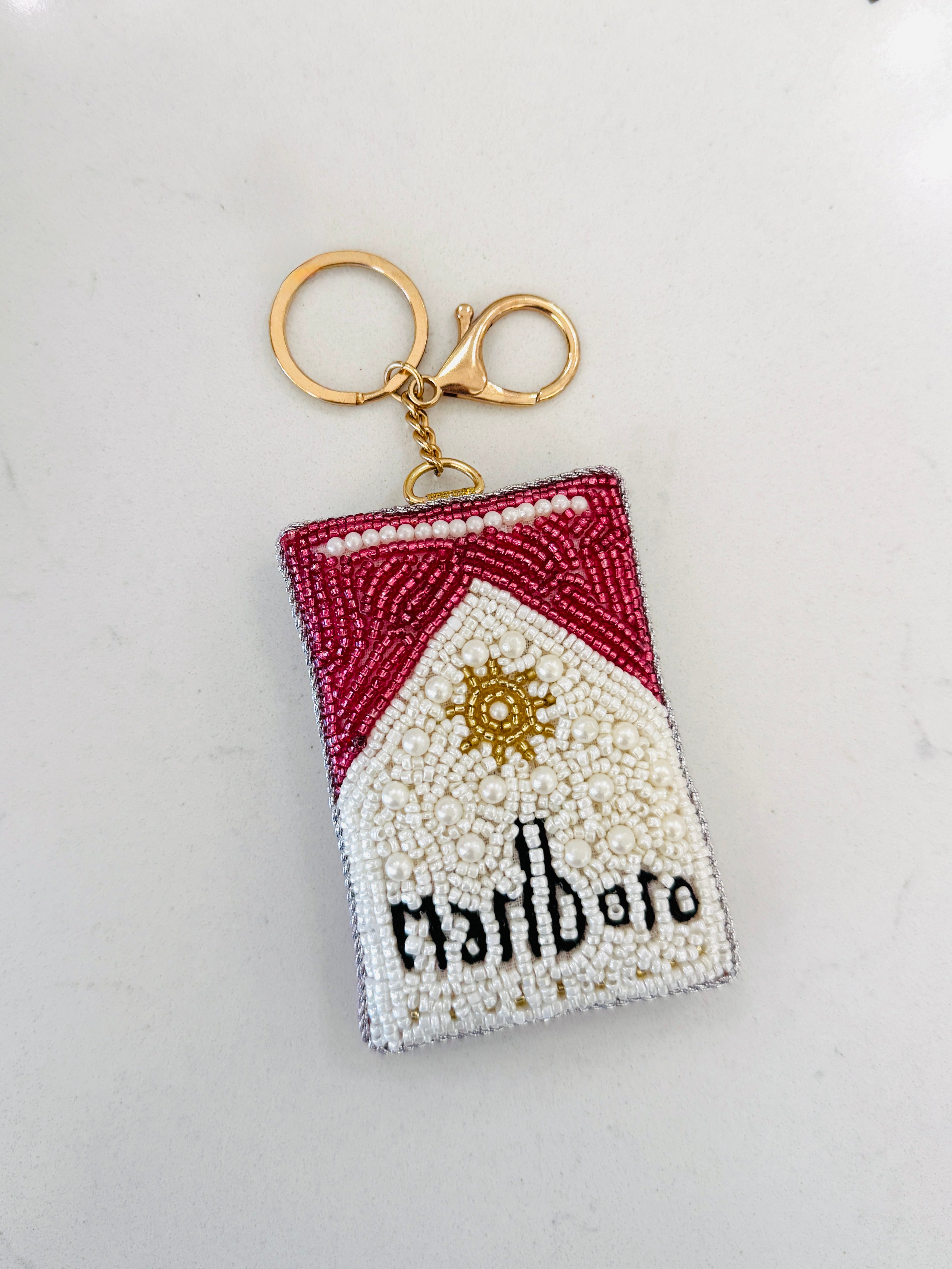 A beaded keychain shaped like a Marlboro cigarette pack, featuring red and white beadwork with a gold-tone metal clasp on a plain white background.