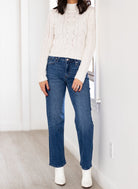 Woman wearing a white sweater and blue jeans standing in a room with white walls.